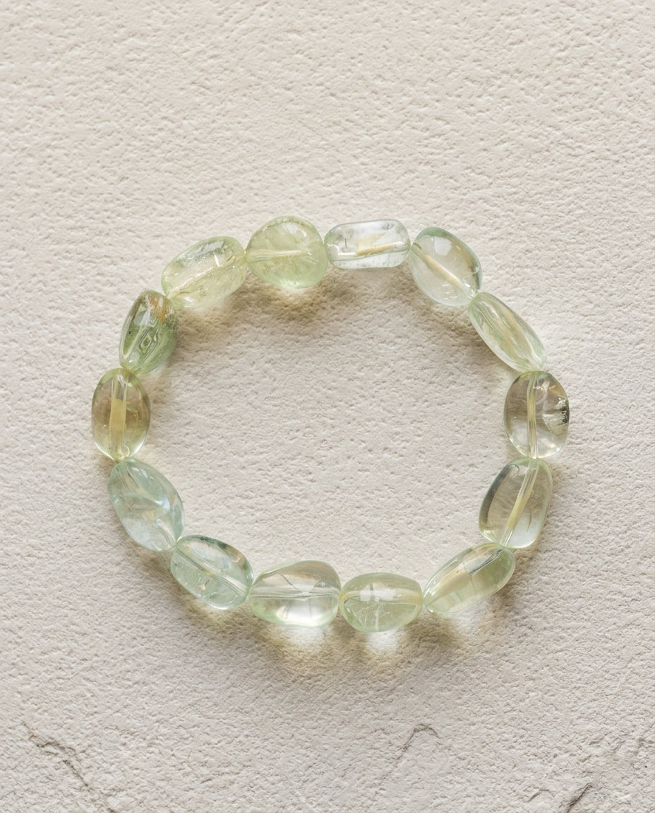 Macro close-up of a natural mixed beryl bracelet showing high transparency pale green, icy blue and yellow organic tumbled crystals, unheated luxury mineral jewelry.