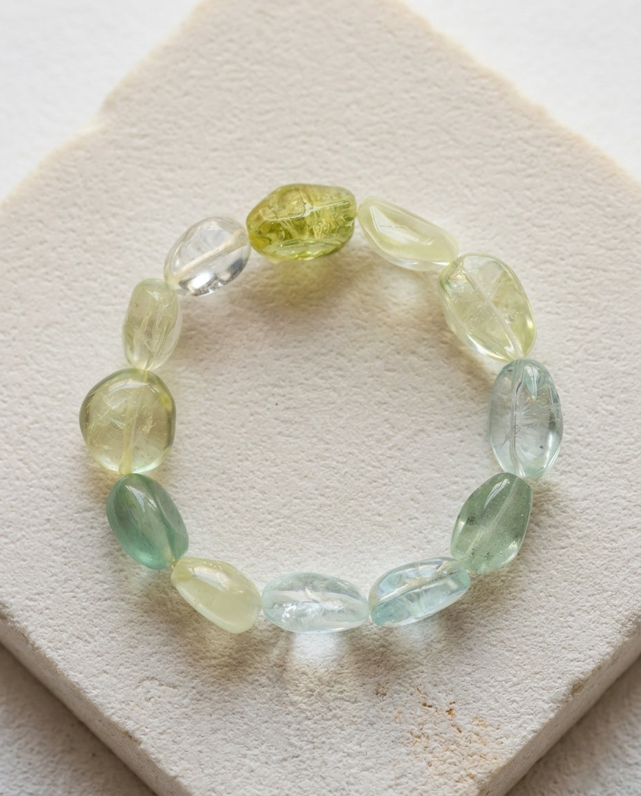 Macro close-up of a massive 45g high transparency mixed beryl bracelet resting on a geometric textured stone plinth, unheated organic cool-toned tumbled crystals.