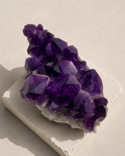 Top-down view of a massive raw Uruguayan Amethyst specimen resting flat on a square architectural concrete plinth, highlighting deep violet crystal terminations and harsh artistic shadows, high-end wabi-sabi mineral decor.