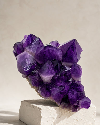 Large deep violet Uruguayan Amethyst crystal cluster displayed on a minimalist textured stone plinth, high-end wabi-sabi interior decor and architectural mineral sculpture.