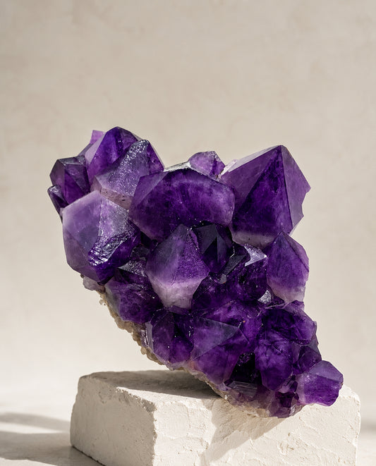 Large deep violet Uruguayan Amethyst crystal cluster displayed on a minimalist textured stone plinth, high-end  interior decor and architectural mineral sculpture.