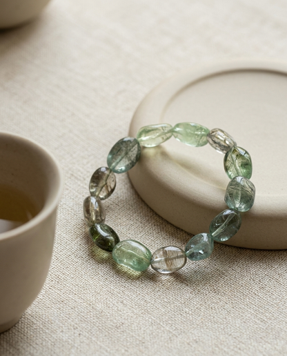 Zero-metal natural green beryl and aquamarine tumbled stone bracelet resting on a wabi-sabi ceramic saucer beside a tea cup, mindful jewelry by STILLMANTLE
