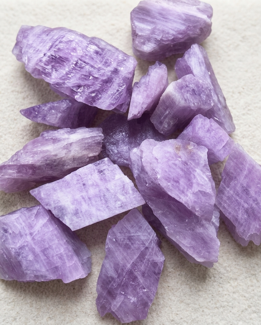 Raw lilac kunzite crystal fragments showing sharp geological cleavage planes on light textured stone, minimalist healing mineral specimen by STILLMANTLE