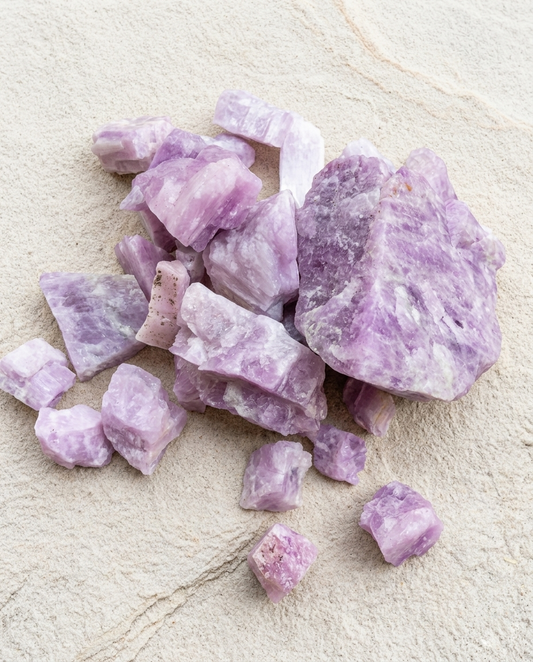 ⁠Unpolished raw kunzite spodumene chunks scattered on a rustic stone slab, soothing purple crystals for wabi-sabi home styling by STILLMANTLE⁠