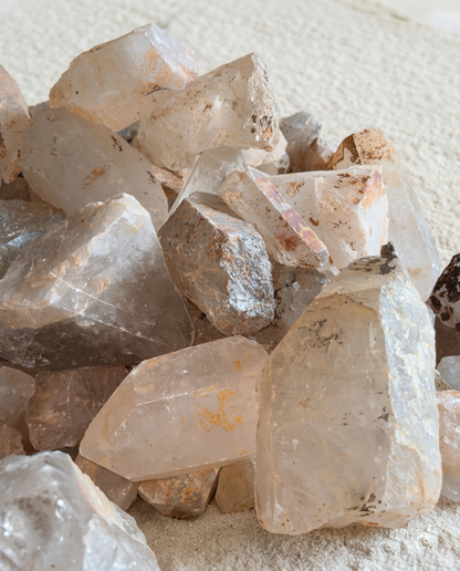 Pile of raw clear quartz crystal points featuring natural iron inclusions and unpolished geometric facets on fine sand, wabi-sabi meditation stones by STILLMANTLE⁠