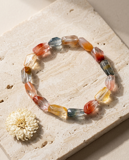 Multicolor faceted angel hair quartz crystal bracelet on textured light stone surrounded by raw clear quartz shards, grounding earth element accessory by STILLMANTLE
