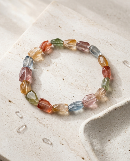 Faceted multicolor amphibole quartz bracelet resting on porous travertine stone beside a dried botanical, wabi-sabi angel hair crystal jewelry by STILLMANTLE