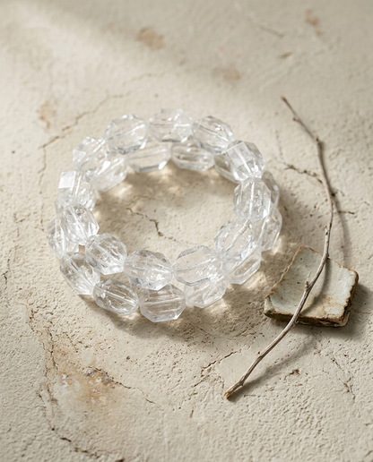 ⁠Close-up of asymmetric faceted clear quartz crystal bracelet on textured light stone, brutalist quiet luxury earth element jewelry by STILLMANTLE⁠