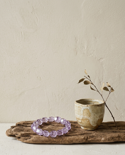 Faceted pale lavender Vera Cruz amethyst bracelet resting on weathered driftwood with a wabi-sabi crackle glaze ceramic cup, rare natural crystal jewelry by STILLMANTLE
