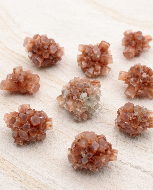 Raw Moroccan Aragonite sputnik crystal clusters with chaotic, terracotta-colored hexagonal formations resting on a textured light stone surface
