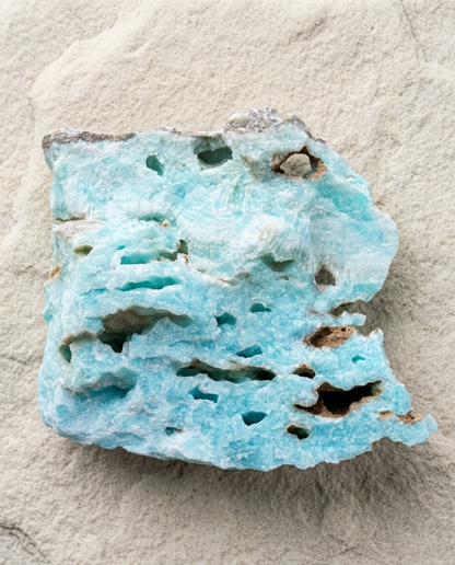 A raw rectangular chunk of vibrant aqua blue Hemimorphite mineral specimen, featuring natural vugs, radiating fibrous textures, and dark brown host rock accents