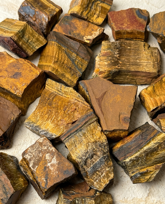 Raw Tiger's Eye stone fragments showing natural golden-brown banding and silky fibrous textures scattered on a light textured surface