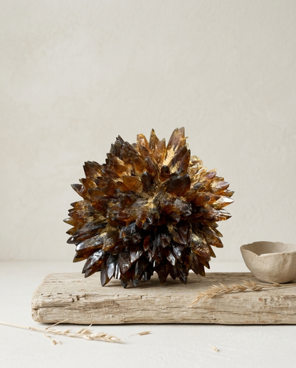 Close-up of a natural Amber Calcite starburst crystal cluster resting on weathered driftwood, accompanied by a wabi-sabi ceramic bowl and dried wheat stalks