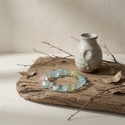 Hand-strung raw pastel mineral bracelet featuring unpolished gemstone fragments, styled on aged driftwood with a rustic ceramic vase, natural raw crystal jewelry design.