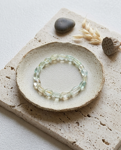 Natural pastel mixed cool-toned beryl bracelet styled on a rustic ceramic plate and textured travertine stone, featuring raw aquamarine and heliodor tumbled nuggets, organic wabi-sabi jewelry aesthetic.