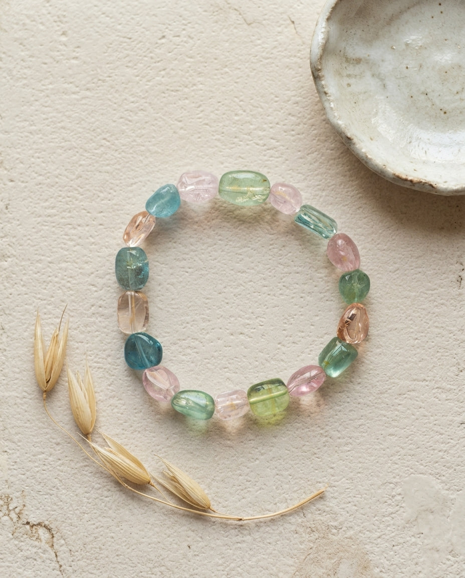 ⁠Macro close-up of a high transparency mixed beryl bracelet resting on a geometric textured stone plinth, unheated organic tumbled crystals.⁠