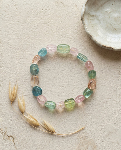 ⁠Macro close-up of a high transparency mixed beryl bracelet resting on a geometric textured stone plinth, unheated organic tumbled crystals.⁠