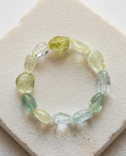 Macro close-up of a massive 45g high transparency mixed beryl bracelet resting on a geometric textured stone plinth, unheated organic cool-toned tumbled crystals.⁠