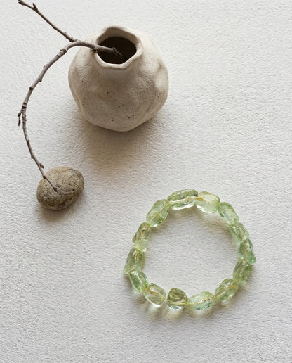 High-clarity natural Green Beryl nugget bracelet, pastel lime-green gemstone jewelry, artisanal minimalist crystal bracelet with organic asymmetrical shapes, isolated on textured stone background.