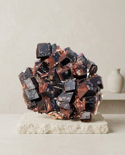 Deep black and red hematite calcite mineral sculpture resting on a raw travertine stone base. Wabi-sabi and organic modern interior styling.⁠