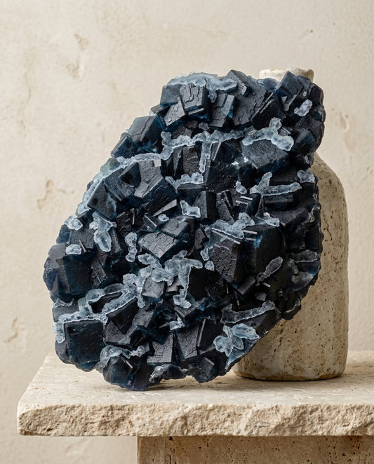 Natural large dark blue cubic fluorite crystal sculpture on travertine base, wabi-sabi minimalist interior decor by STILLMANTLE.⁠