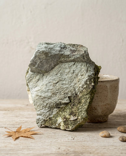 Reverse matrix side of a raw Turkish epidote specimen, revealing the rugged grey host rock alongside minimalist ceramics. Organic modern decor.⁠